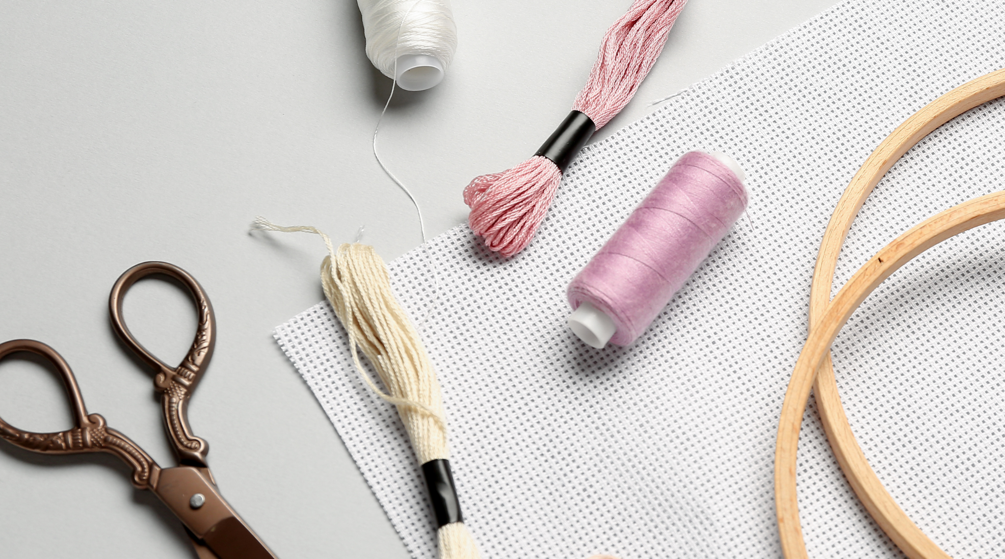 Embroidery supplies including scissors, thread, and hoops on a light gray background